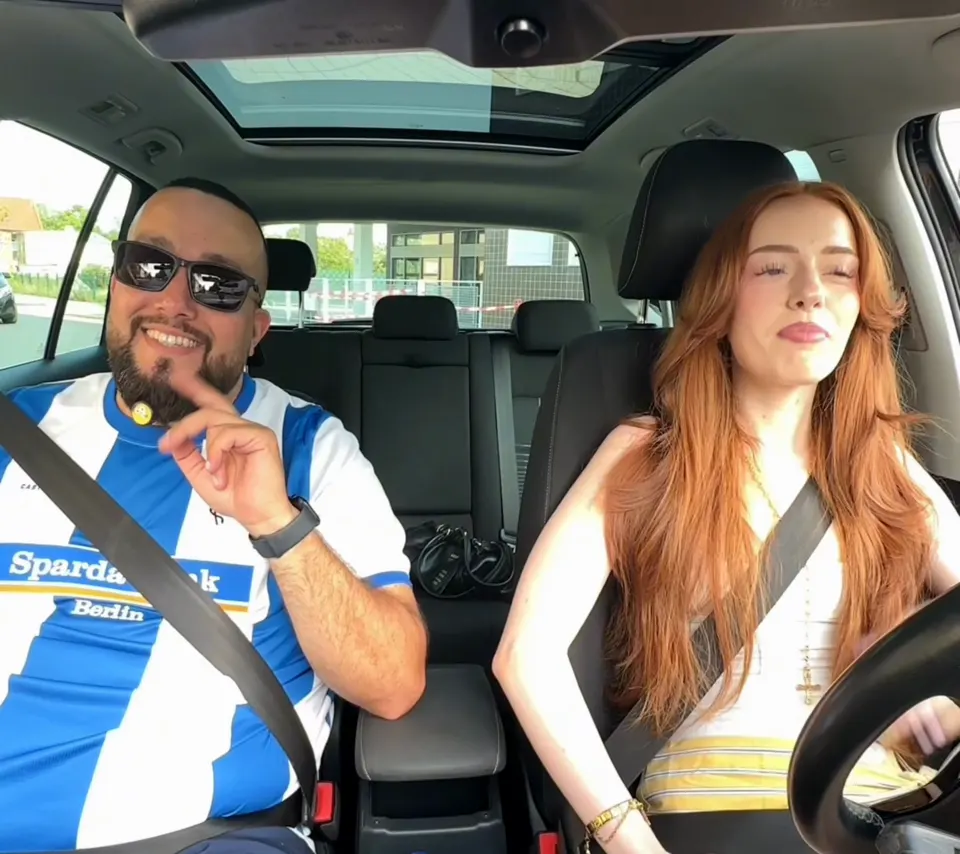 Tolga lacht mit seiner Fahrschülerin während einer Fahrstunde