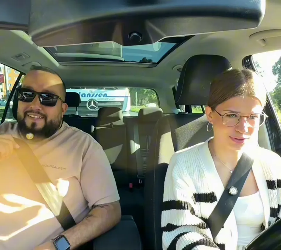 Tolga mit Sonnenbrille und seine Fahrschülerin lächeln während der Fahrt